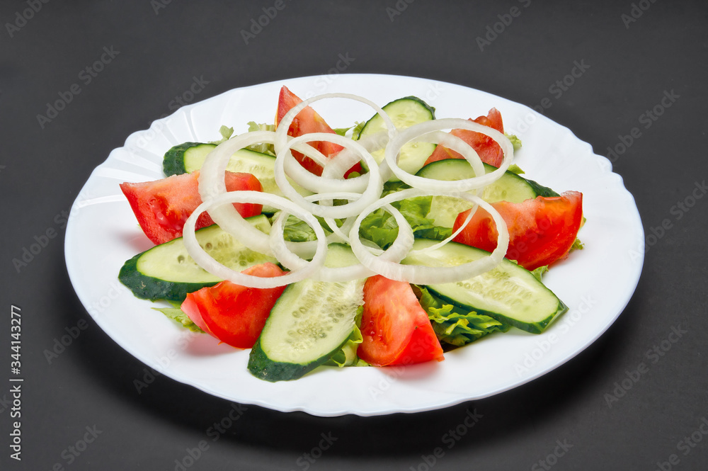 White ceramic plate with fresh cucumber, tomato and onion salad on grey background White ceramic plate with fresh cucumber, tomato and onion salad on grey background