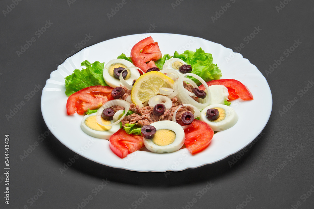 White ceramic plate with fresh tomatoes, onion, eggs, olives and fish salad on grey background