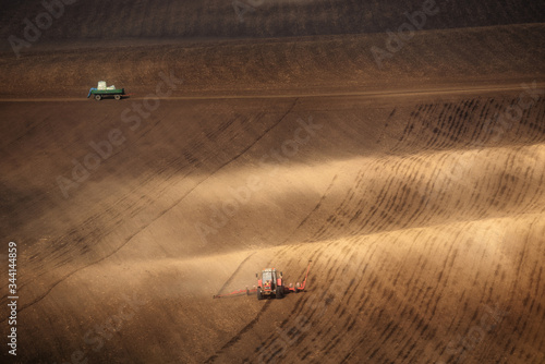 Red tractor working on brown hills of South Moravia, Czech Republic. Spring rural landscape with brown fields and a red tractor