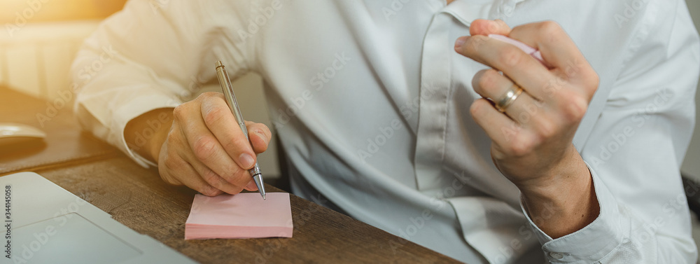 Obraz premium Close up of a man sitting at the desk holding a pen and writing in a post it then throw it in wastepaper.