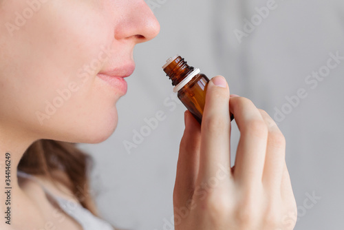 Aromatherapy: a girl with beautiful skin holds a bottle of essential oil near her nose and inhales. Close up, bright marble background. photo