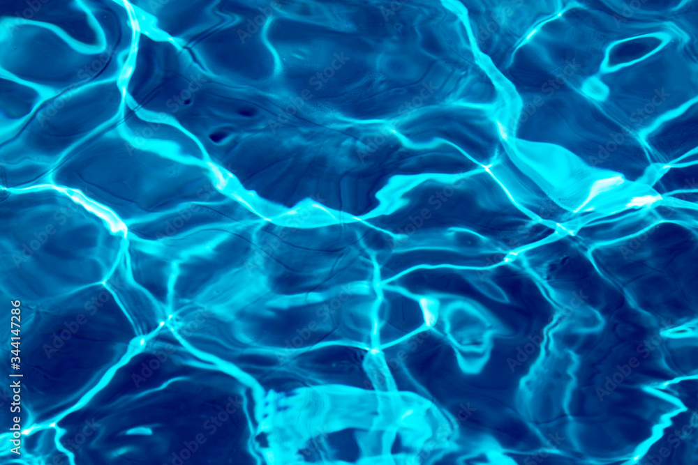 ripple water in swimming pool with sun reflection. blue water background texture