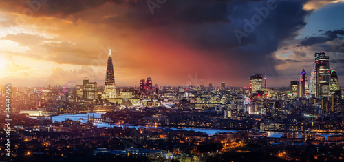Blick auf die beleuchtete Skyline von London während eines farbenfrohen Sonnenunterganges mit Wolken und Regen, Großbritannien