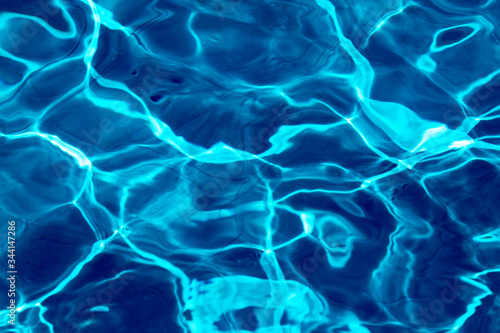 ripple water in swimming pool with sun reflection. blue water background texture