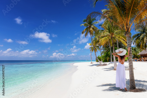 Tropisches Reisebanner mit einer Frau mit weißem Hut die an einem tropischen Traumstrand mit Palmen und türkisem Meer steht und die Aussicht genießt, Malediven © moofushi