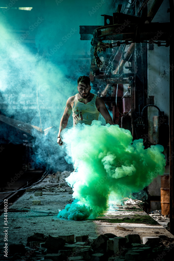Fototapeta premium a man with a sports figure in the factory confidently passes through green smoke.