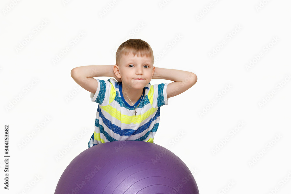 The child is engaged with a large gymnastic ball. Fitness exercises at home during a pandemic. Boy on the ball Isolated on a white background. The child is engaged with a large gymnastic ball. Fitness exercises at home during a pandemic. Boy on the ball Isolated on a white background.