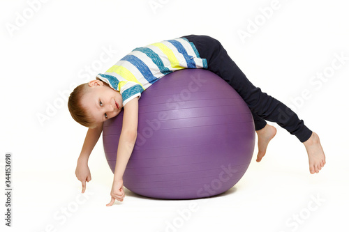 The child is engaged with a large gymnastic ball. Fitness exercises at home during a pandemic. Boy on the ball Isolated on a white background.