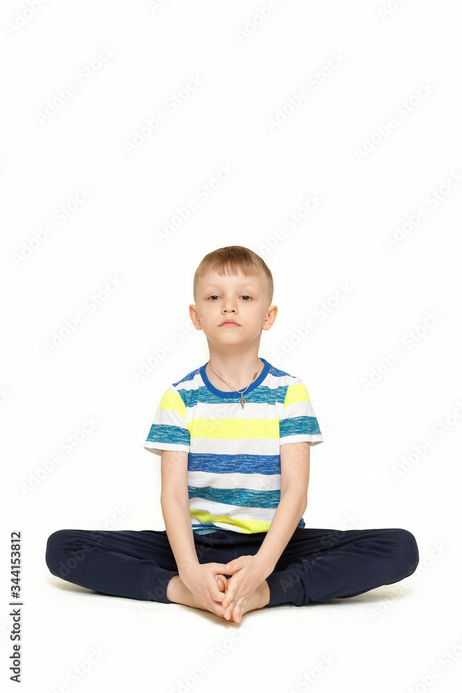 The child does gymnastic exercises for muscle stretching. Gymnastics at home during a pandemic. The boy goes in for sports Isolated on a white background. The child does gymnastic exercises for muscle stretching. Gymnastics at home during a pandemic. The boy goes in for sports Isolated on a white background.
