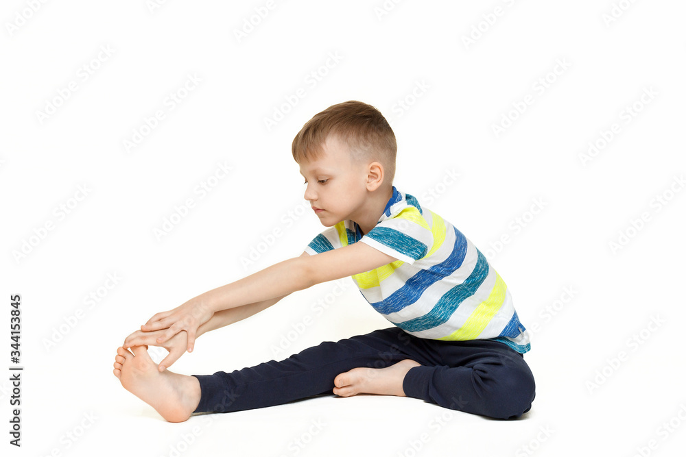 The child does gymnastic exercises for muscle stretching. Gymnastics at home during a pandemic. The boy goes in for sports Isolated on a white background. The child does gymnastic exercises for muscle stretching. Gymnastics at home during a pandemic. The boy goes in for sports Isolated on a white background.
