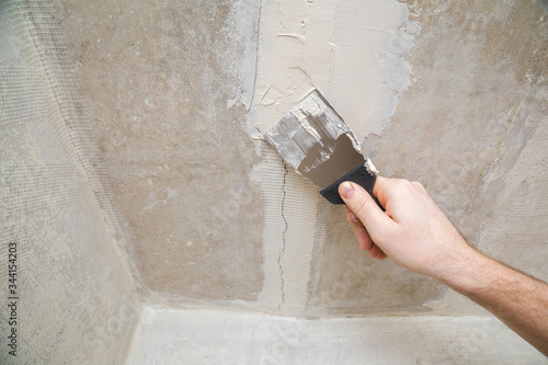 Worker hand using spatula and plastering ceiling with putty. Mesh on split. Closeup. photo