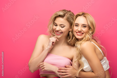 Beautiful blonde woman hugging smiling friend on pink background