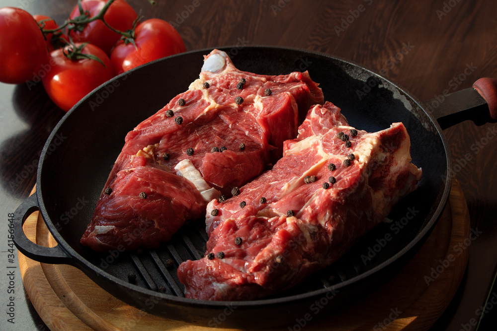 Two raw beef steaks on a bone in a grill pan seasoned with pepper and tomatoes.