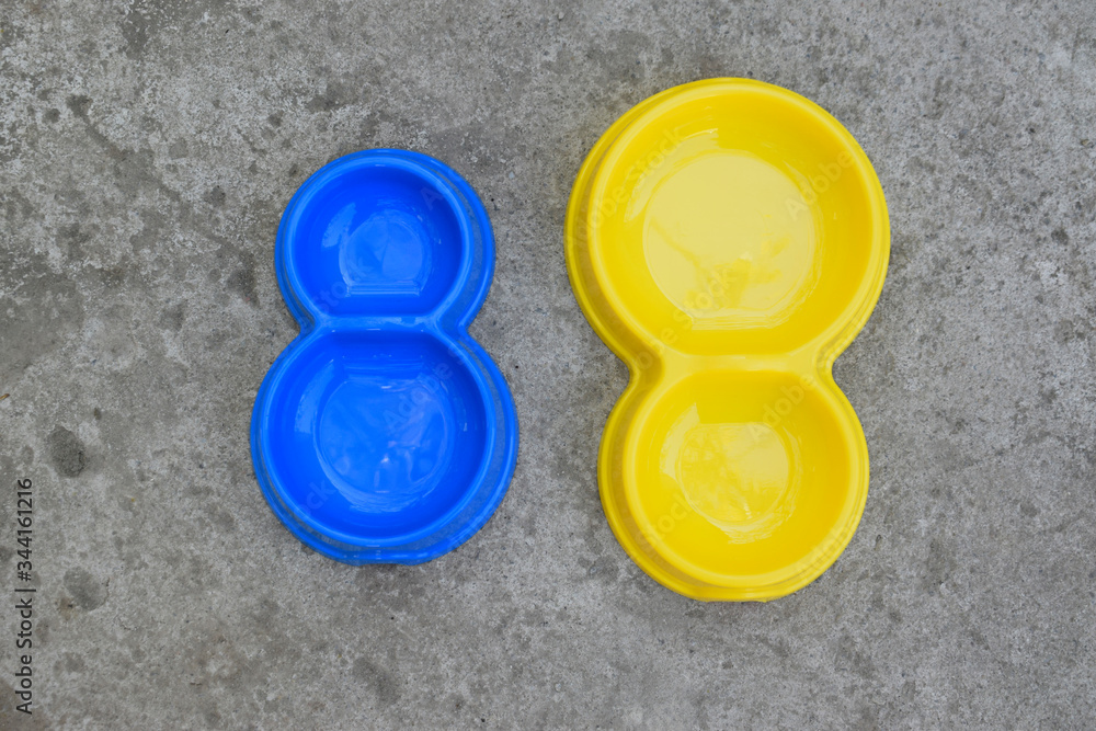 Two double plastic pet bowls in blue and yellow. Empty bowls on concrete background. View from above.