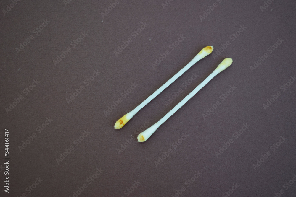 Two cotton ear buds smeared with earwax on a dark background, top view. Two cotton ear buds smeared with earwax on a dark background, top view.