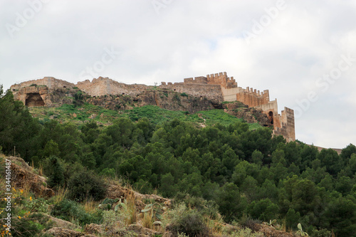 Walls and towers of old medieval Sagunto impregnable fortress ruin on a hill in Spain surrounded by green forest © Sergei Timofeev