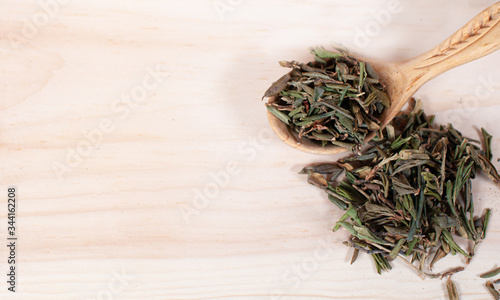 dry black tea with mountain herbs scattered on a light background with a wooden spoon. healthy eating concept copy spase.