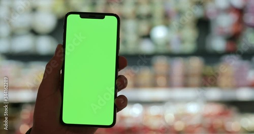 Close up view of hand holding modern smartphone with template mock up screen. Bokha blurred lights at background.Concept of chroma key and green screen. Indoors photo