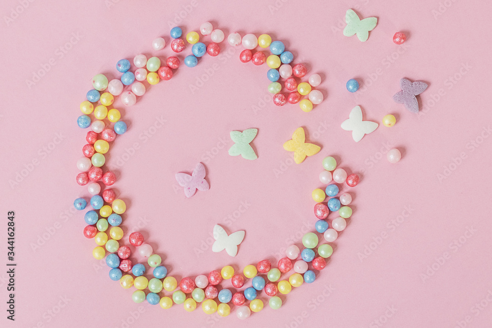 Pastry sprinkles are scattered in the form of a ragged circle, with multicolored butterflies flying out of it on a pink background Pastry sprinkles are scattered in the form of a ragged circle, with multicolored butterflies flying out of it on a pink background