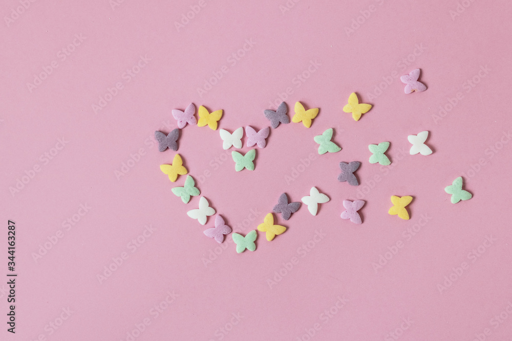Pastry multicolored sprinkles-butterflies are laid out in the form of a decaying heart on a pink background. Decoration of confectionery products.