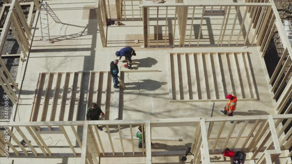Top ascending aerial view of working builders team, zooming out view of wooden frame house under construction