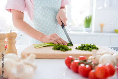 Cropped close-up view of her she hands girl making meal cutting green vitamin weight loss salad on wooden board cutter table desk in modern white light interior style kitchen indoors