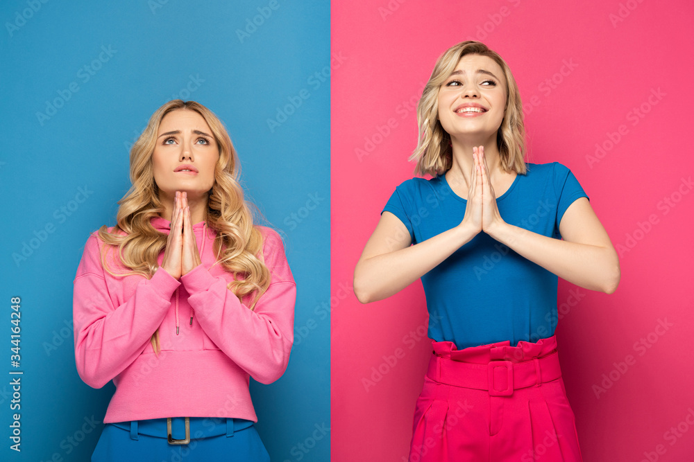 Blonde sisters with prayer hands looking away on pink and blue background Blonde sisters with prayer hands looking away on pink and blue background