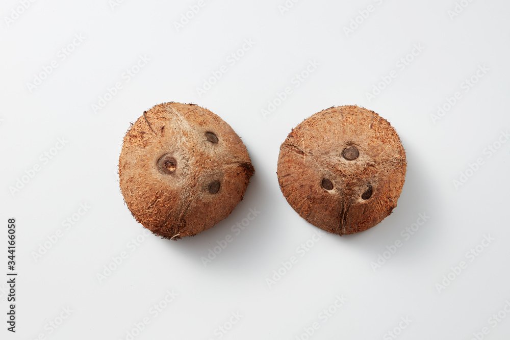 Two whole parts of brown natural tropical coconut fruit on a grey background. Two whole parts of brown natural tropical coconut fruit on a grey background.