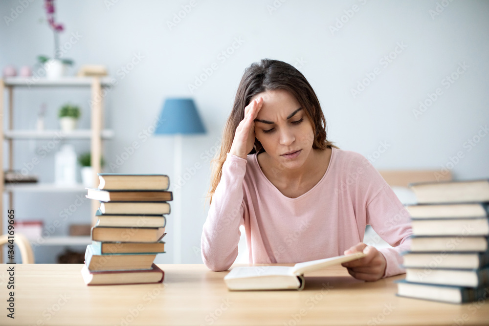 Sad female student reading a book for the exam or doing homework. Sad female student reading a book for the exam or doing homework.