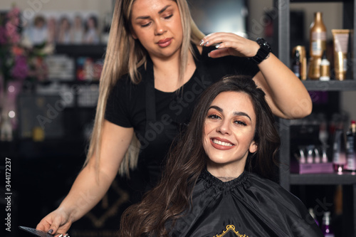 Female hairdresser makes hairstyle on young woman with brunette hair in salon. 