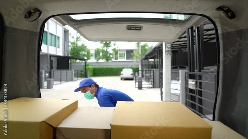 Corona Virus concept.Blue delivery handsome asian man wearing protection mask and medical rubber gloves puts cardboard boxes in the trunk of a car. Volunteer work in the midst of an epidemic. 4k resol photo