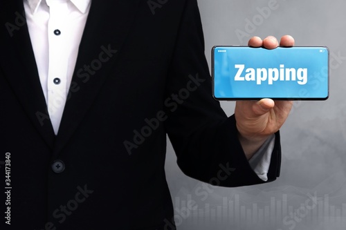 Zapping. Geschäftsmann im Anzug hält ein Smartphone in die Kamera. Der Begriff Zapping steht auf dem Handy. Konzept für Business, Finanzen, Statistik, Analyse, Wirtschaft photo