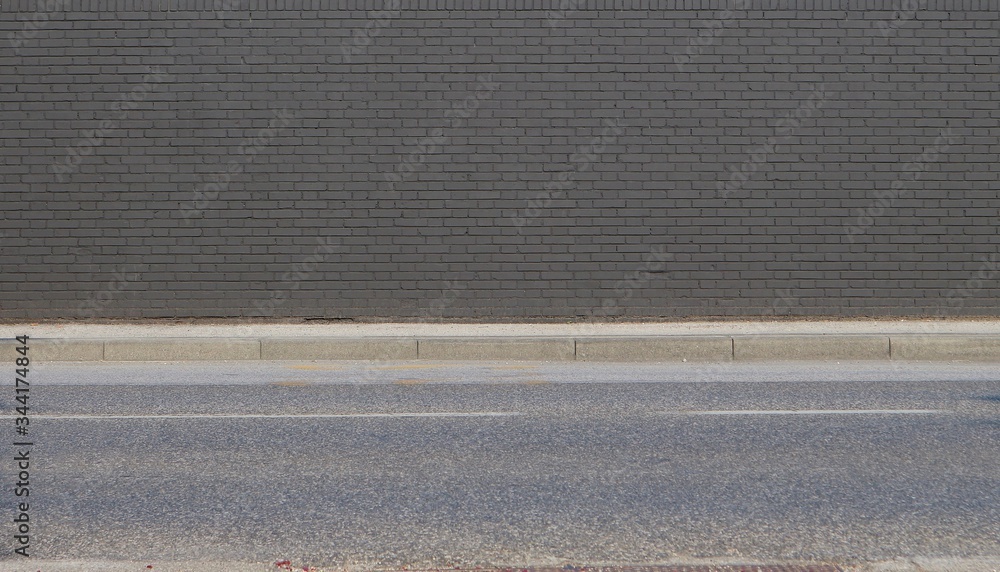 Fototapeta premium Gray painted brick wall with concrete sidewalk and asphalt road in front. Background for copy space.