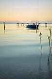 Ruhiger See mit sanften Wellen, Schilf und einem dekorativen Steg und einem blauen Boot