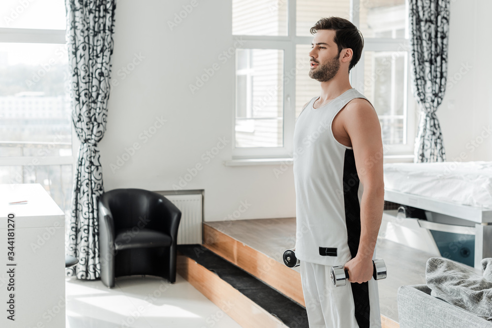 Fototapeta premium Handsome man holding barbells while training at home