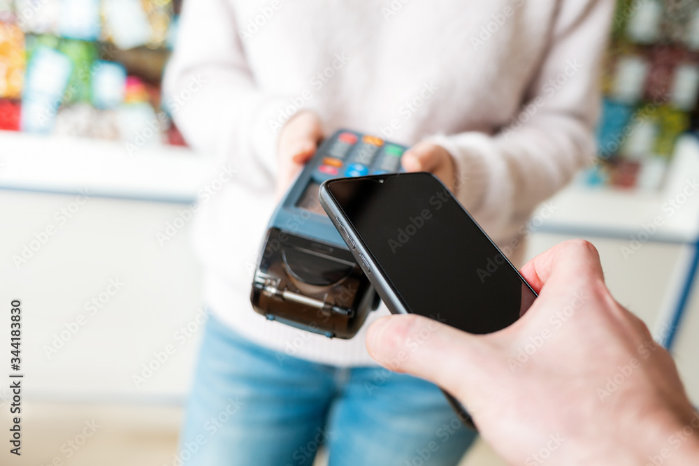 The seller holds a payment terminal, and the man pays for the purchase using a smartphone, online. Top view. Copy space. NFC concept, business and banking operations The seller holds a payment terminal, and the man pays for the purchase using a smartphone, online. Top view. Copy space. NFC concept, business and banking operations