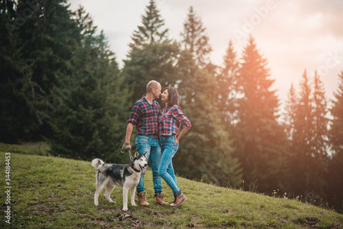 Romantic traveling couple walking with husky dog in the mountains. Caucasian man and woman in love in mountains at sunset. Portrait of a happy couple smile to camera. Lifestyle concept. Banner