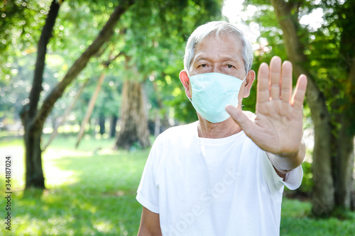 An elderly man is wearing a green cloth mask, raise your hand, do not get close to prevent the spread of the virus. Coronavirus Prevention Concept, Social Distance