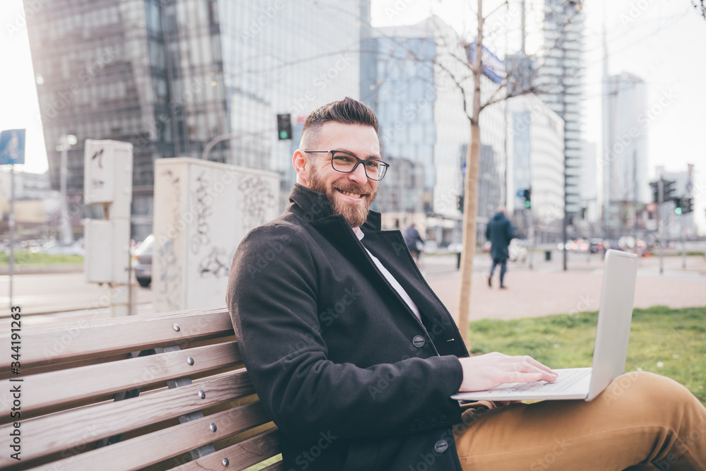 Young handsome caucasian smart man outdoors sitting bench using computer smiling Young handsome caucasian smart man outdoors sitting bench using computer smiling