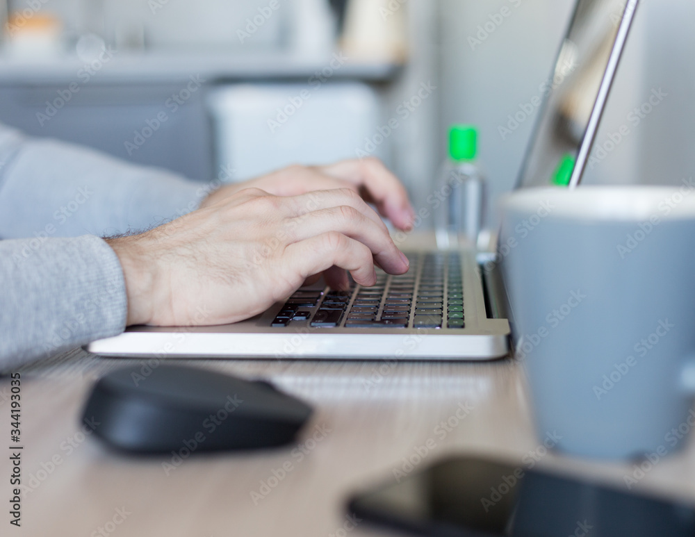 Young man working at home with a laptop with bottle of sanitize on table. Stay home concept. Home office with sanitizer and cup of tea Young man working at home with a laptop with bottle of sanitize on table. Stay home concept. Home office with sanitizer and cup of tea