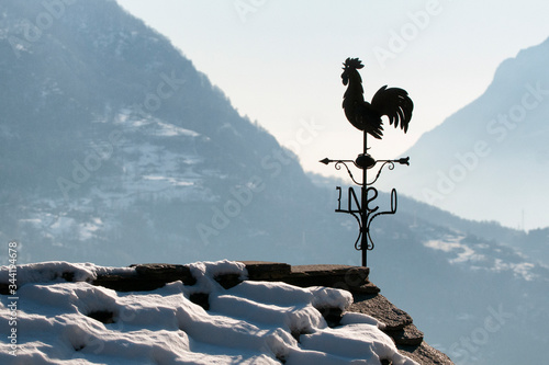 Bilde på lerret Rooster wind vane on the snowy roof of a house in Aosta in Italy
