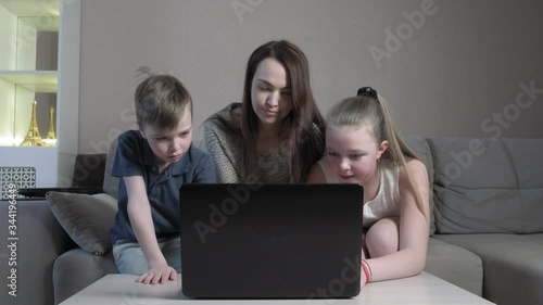 Focused cute boy and girl and their mom using laptop study online in app typing on computer exam sit at home sofa during the COVID 19 pandemic.