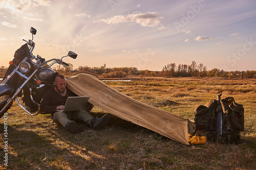 A traveler on a motorcycle talking on the phone working on a laptop admires the sunset