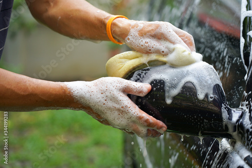Hand of man holding sponge and foam washing car closedup image