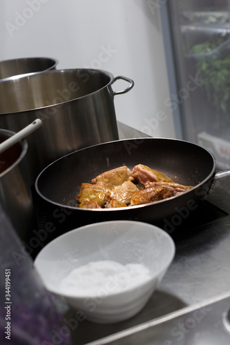 tegame con della carne in cottura in mezzo ad altre pentole nei fornelli di una cucina