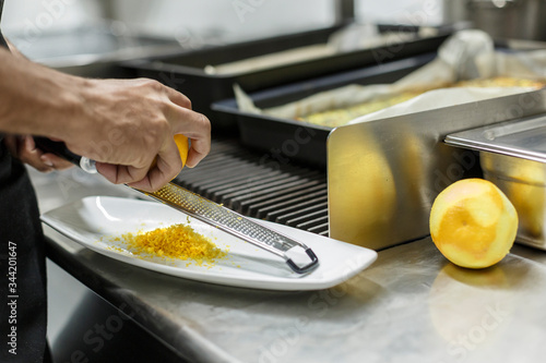 Cuoco grattugia la buccia del limone in un piatto bianco in cucina photo