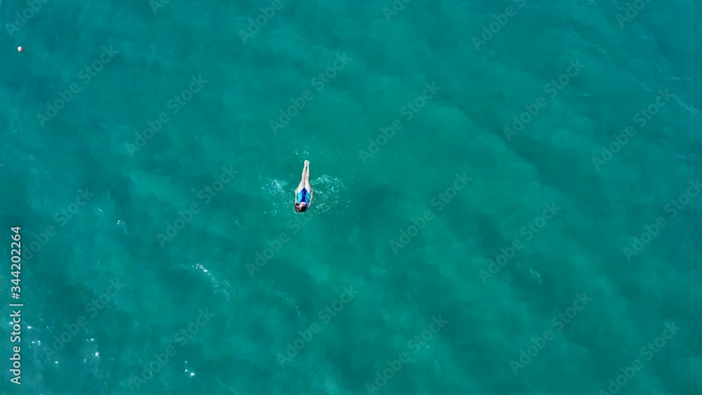 Aerial view of a young girl floating in the transparent sea. The girl is swimming alone, there are no people around, the sea is calm. Taken by drone on a summer day in Cyprus, looking down Aerial view of a young girl floating in the transparent sea. The girl is swimming alone, there are no people around, the sea is calm. Taken by drone on a summer day in Cyprus, looking down
