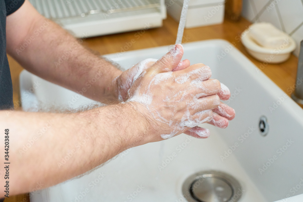 Man washing hands with soap by the kitchen sink. Adult person preventing virus spread. Personal hygiene