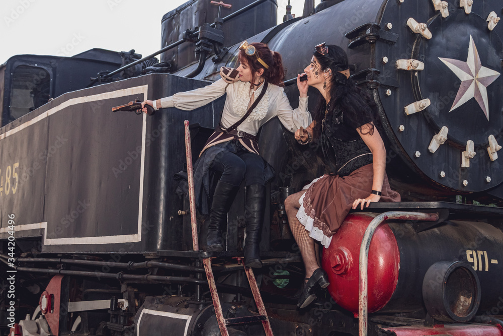 Fototapeta premium Two beautiful girl in steampunk clothes on the background of the train