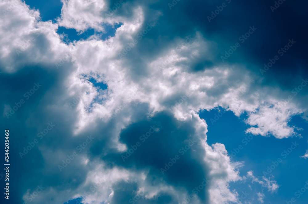 Blue sunny sky covered by black clouds.